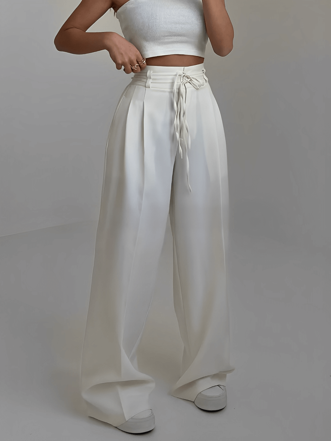 Modelo vestindo calça alfaiataria Paulina na cor off white, modelagem wide leg de cintura alta com detalhe de amarração frontal e pregas elegantes