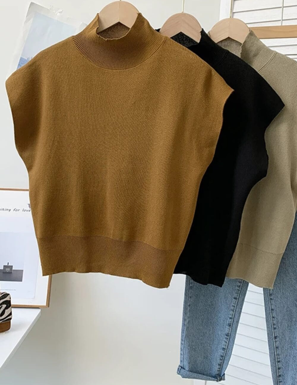 Modelo vestindo regata de tricô gola alta na cor camel, com ombros estruturados estilo muscle tee e modelagem soltinha na cintura