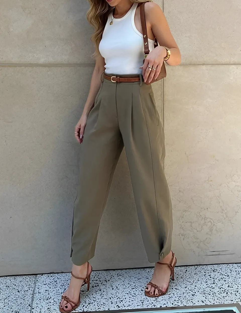 Modelo vestindo Calça Ester de alfaiataria slim na cor verde militar, com cintura média, pregas frontais elegantes e cinto fino ajustável na cintura