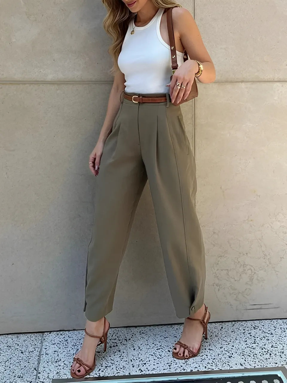 Modelo vestindo Calça Ester de alfaiataria slim na cor verde militar, com cintura média, pregas frontais elegantes e cinto fino ajustável na cintura