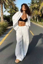 Modelo na praia vestindo Conjunto Dakota de algodão branco, composto por camisa oversized aberta e calça pantalona larga com amarração na cintura