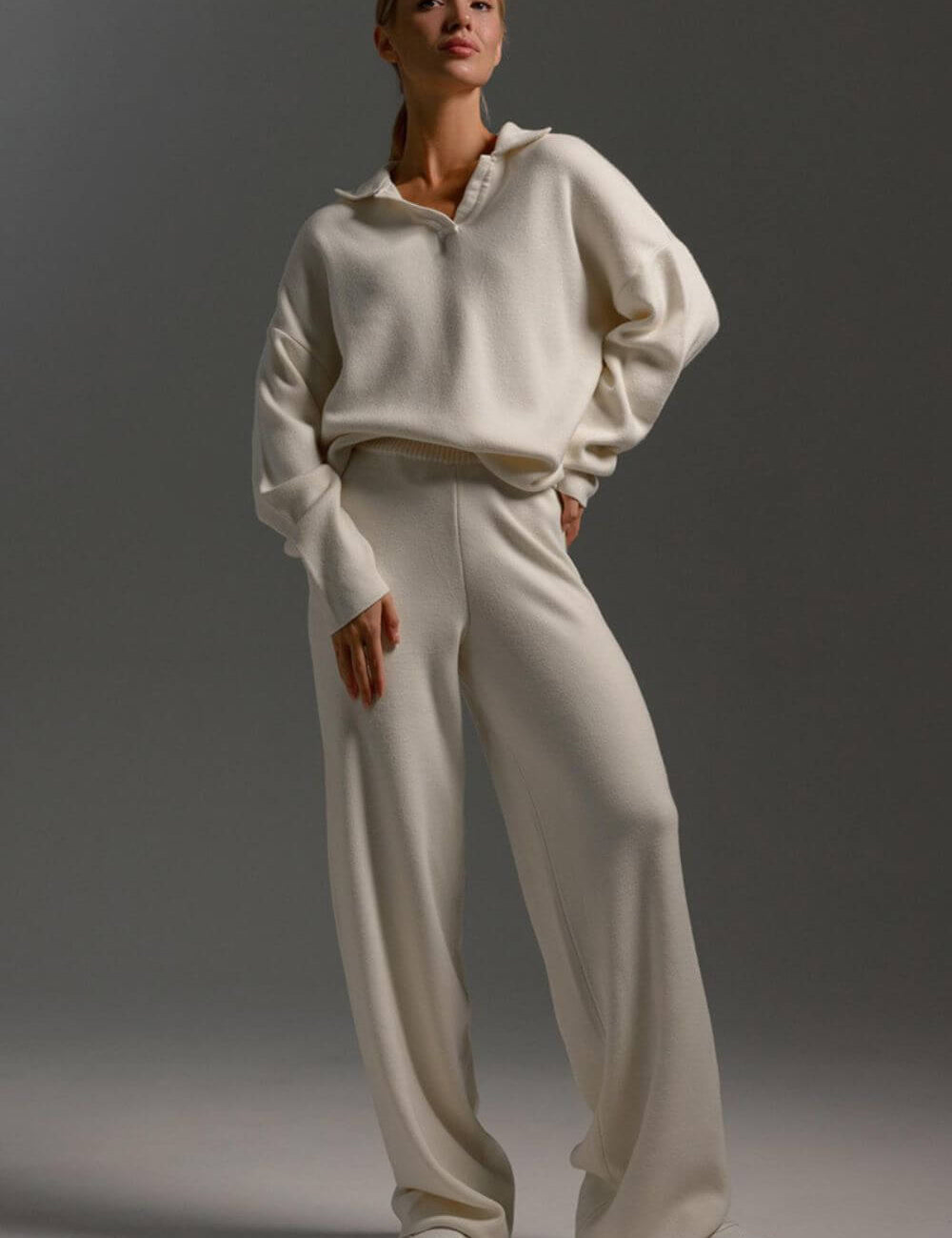 Modelo vestindo Conjunto Clarice de tricô off-white, composto por blusão oversized de mangas longas com gola polo aberta e calça pantalona solta.