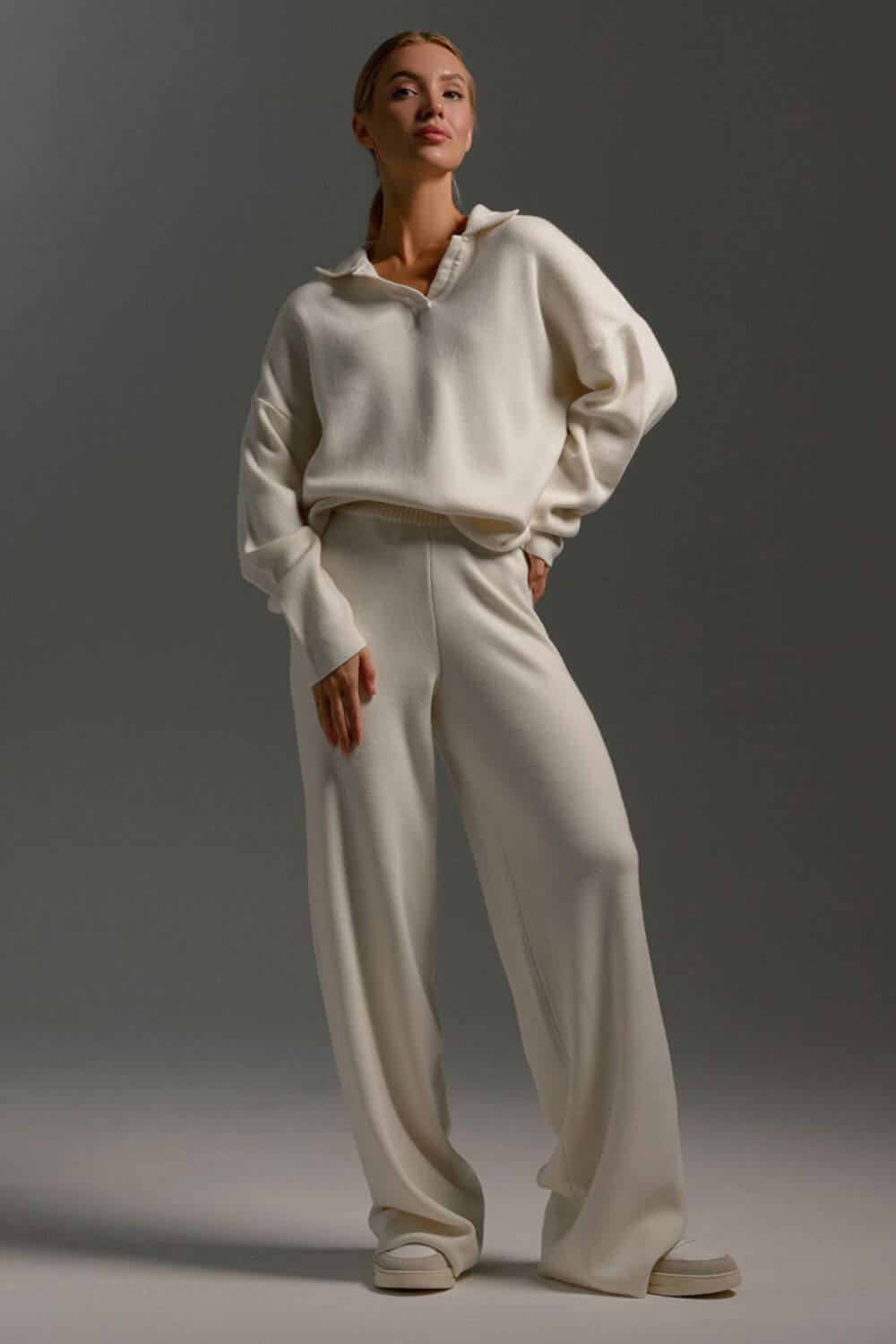 Modelo vestindo Conjunto Clarice de tricô off-white, composto por blusão oversized de mangas longas com gola polo aberta e calça pantalona solta.