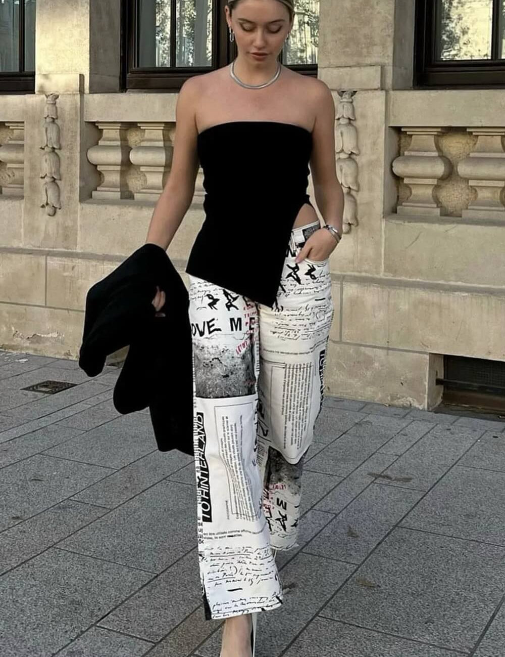 Modelo vestindo Top Lindsay preto tomara que caia, justo ao corpo, com uma fenda lateral profunda na cintura e barra assimétrica pontuda.