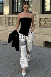 Modelo vestindo Top Lindsay preto tomara que caia, justo ao corpo, com uma fenda lateral profunda na cintura e barra assimétrica pontuda.