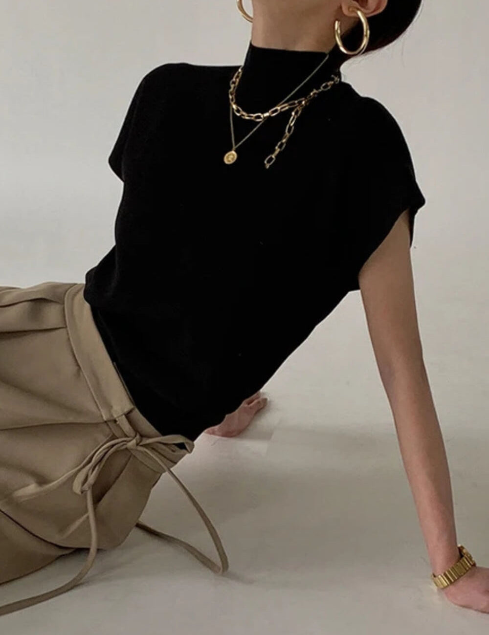 Modelo vestindo regata de tricô gola alta na cor camel, com ombros estruturados estilo muscle tee e modelagem soltinha na cintura