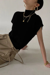 Modelo vestindo regata de tricô gola alta na cor camel, com ombros estruturados estilo muscle tee e modelagem soltinha na cintura