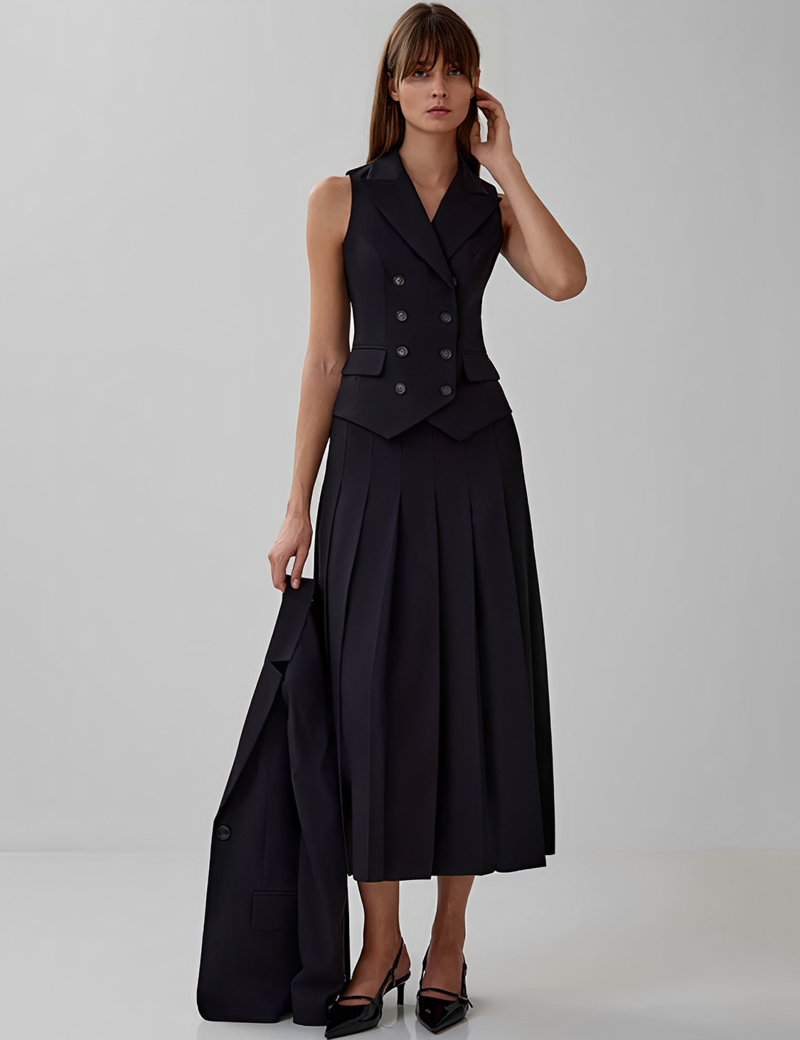 Modelo vestindo conjunto Lizandra all black de alfaiataria, com colete de botões duplos e saia midi plissada de caimento estruturado