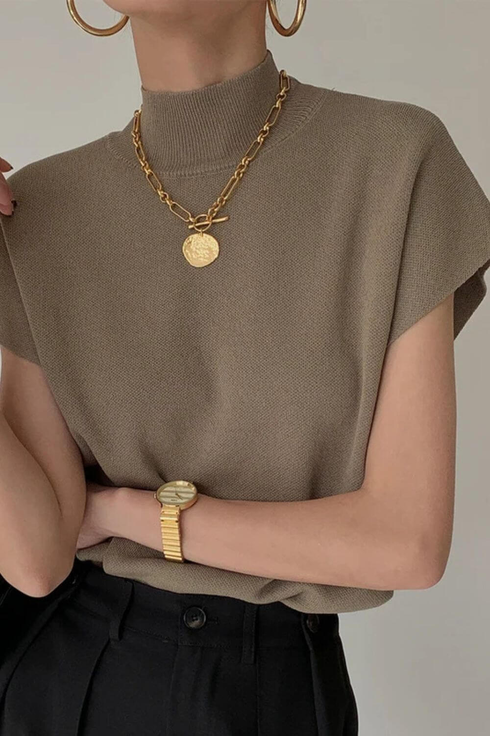 Modelo vestindo regata de tricô gola alta na cor camel, com ombros estruturados estilo muscle tee e modelagem soltinha na cintura