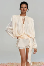 "Modelo vestindo Vestido Giulieta curto em tecido acetinado com textura amassadinha (crushed), mangas longas bufantes volumosas e saia de babados em camadas.