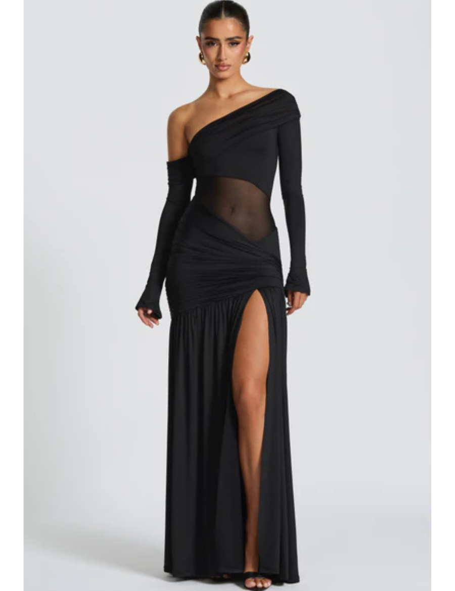 Modelo vestindo Vestido Seraphine longo preto de um ombro só, confeccionado em malha slinky com recorte transparente na cintura e fenda profunda na perna.