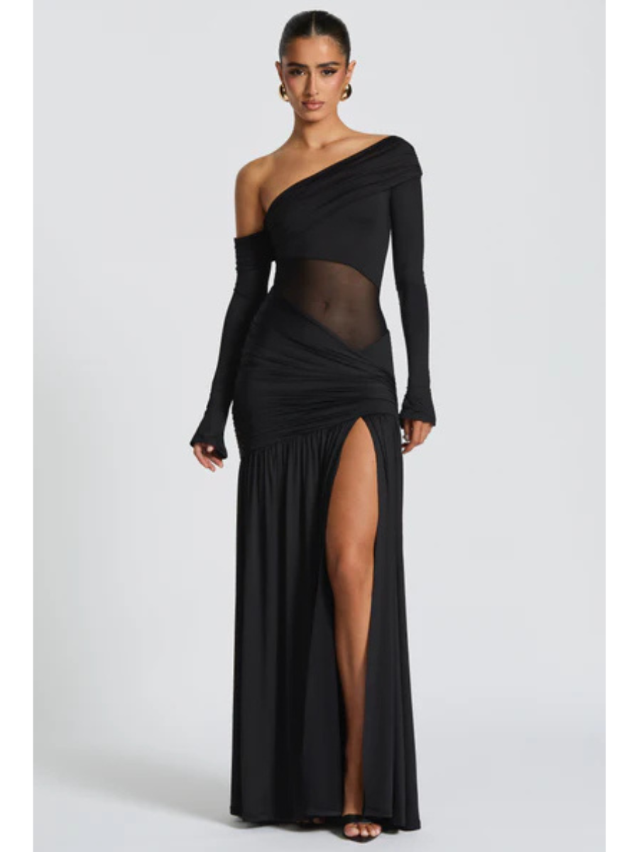 Modelo vestindo Vestido Seraphine longo preto de um ombro só, confeccionado em malha slinky com recorte transparente na cintura e fenda profunda na perna.