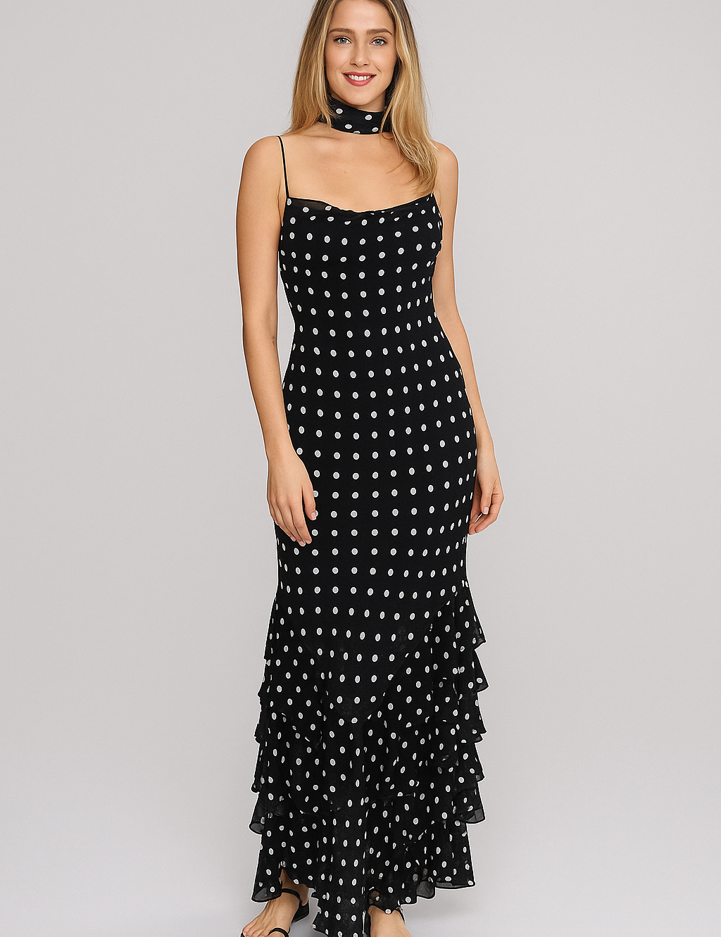 Modelo loira em evento noturno usando Vestido Sofi longo preto com bolinhas brancas (poá), alças finas, babados na barra e lenço no pescoço combinando