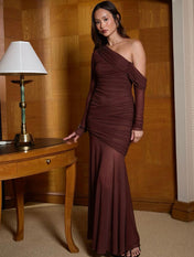 Modelo em ambiente sofisticado vestindo Vestido Sienna longo de tule drapeado, design de um ombro só com manga longa transparente e forro interno ajustado.