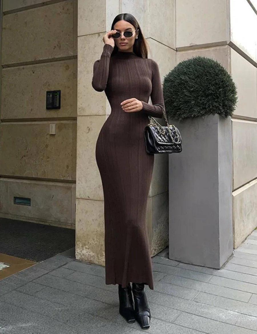 Modelo vestindo Vestido Amira marrom café, comprimento midi alongado, tecido canelado ajustado ao corpo, gola alta e mangas longas, estilo minimalista elegante.